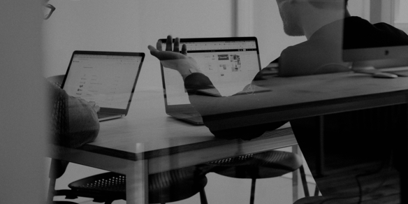 Schwarz-Weiß-Foto eines Entwicklers an zwei Laptops in einer dunklen Umgebung