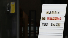 Weißes Stecktafel-Schild mit der Aufschrift „Happy to Welcome You Back" am Eingang eines Gebäudes