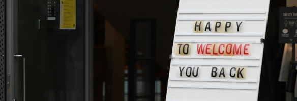Weißes Stecktafel-Schild mit der Aufschrift „Happy to Welcome You Back" am Eingang eines Gebäudes
