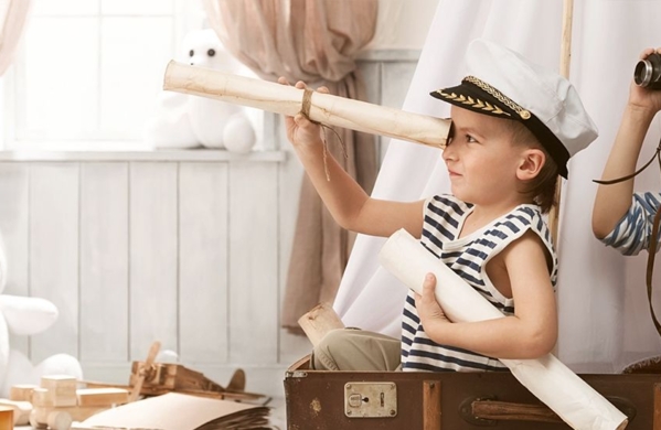 Kinder in Matrosenkleidung spielen mit Fernglas und Fernrohr in einem gemütlichen Zimmer.