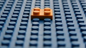 Einzelner orangefarbener Legostein hebt sich von blauer Lego-Grundplatte ab