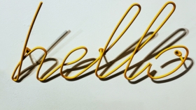 Gelber Drahtschriftzug „Hello" an einer weißen Wand mit Schatten