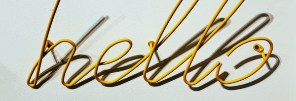 Gelber Drahtschriftzug „Hello" an einer weißen Wand mit Schatten