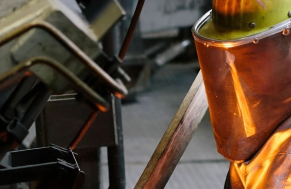 Person in Schutzkleidung mit orangefarbenem Gesichtsschutzhelm in einer Industrieumgebung