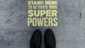 Vogelperspektive auf Asphalt Schuhspitzen mit Stencilspruch: Stand here to activate your superpower