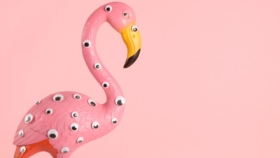 Rosa Flamingo-Figur mit aufgeklebten Wackelaugen vor pastellrosa Hintergrund