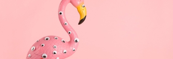 Rosa Flamingo-Figur mit aufgeklebten Wackelaugen vor pastellrosa Hintergrund