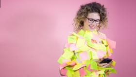 Lächelnde Frau blickt auf ihr Smartphone und ist übersäht mit zahlreichen bunten PostIts
