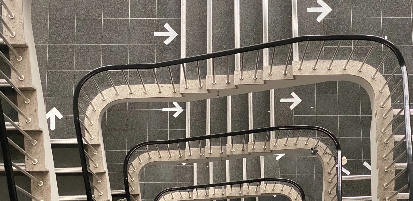 Blick von oben runter in ein Treppenhaus mit wegweisenden Pfeilen auf den Etagenboeden