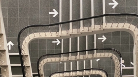 Blick von oben runter in ein Treppenhaus mit wegweisenden Pfeilen auf den Etagenboeden