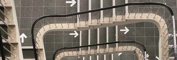 Blick von oben runter in ein Treppenhaus mit wegweisenden Pfeilen auf den Etagenboeden