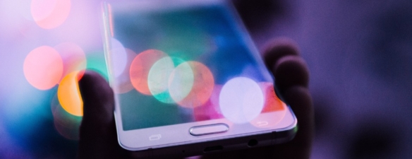 Hand haelt ein Smartphone mit bunten Bokeh-Lichtern, symbolisiert digitale Mobile-Erfahrung
