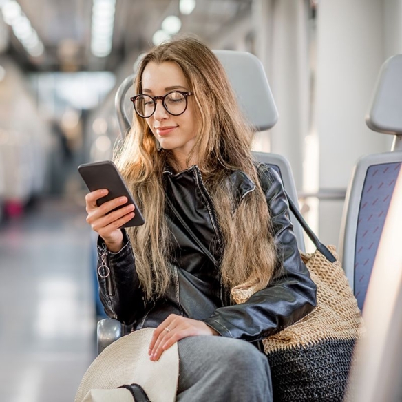 Frau mit Brille schaut auf ihr Smartphone in oeffentlichen Verkehrsmitteln, symbolisiert digitale Nutzererfahrung