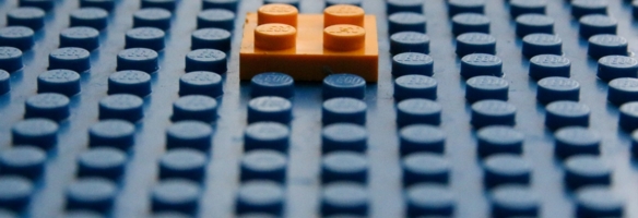 Einzelner orangefarbener Legostein hebt sich von blauer Lego-Grundplatte ab