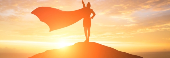 Menschliche Silhouette in Superhelden-Pose mit Umhang auf einem Berggipfel im Sonnenuntergang