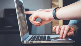 Hände deuten aus seitlicher Betrachtung auf einen Laptopbildschirm
