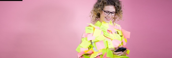 Lächelnde Frau blickt auf ihr Smartphone und ist übersäht mit zahlreichen bunten PostIts