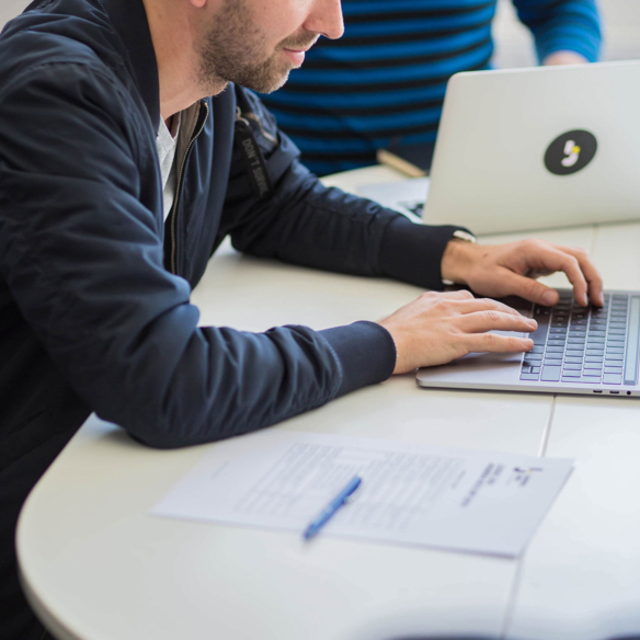 Logic Joe Managing Director arbeitet konzentriert am Laptop, Dokumente auf dem Tisch
